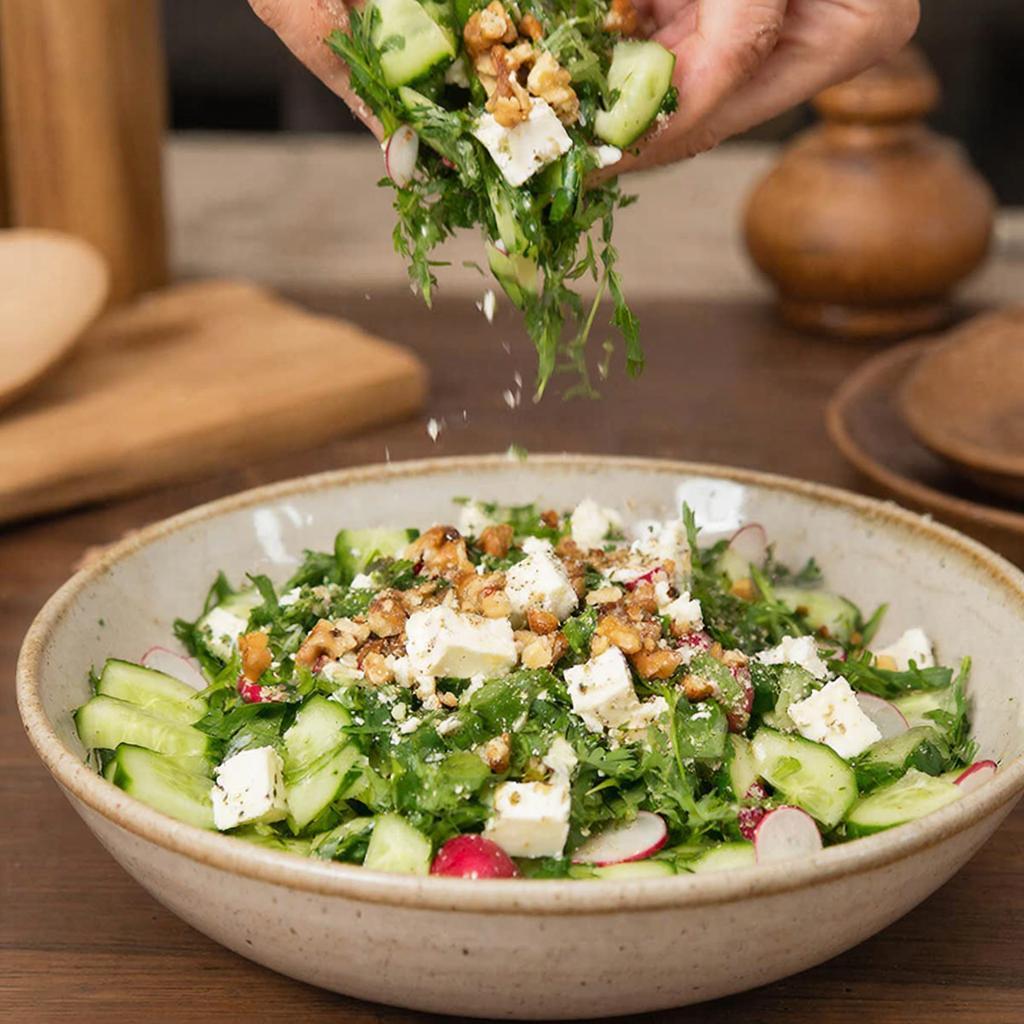 Сборка салата с фетой Смешивание салата с огурцом, редисом, фетой, зеленью и грецкими орехами в большой миске